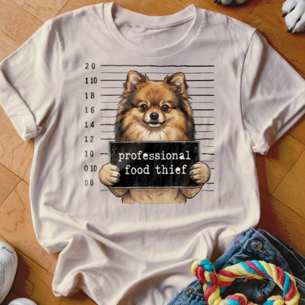 T-shirt graphic of a Pomeranian dog holding a "professional food thief" sign in a mugshot.