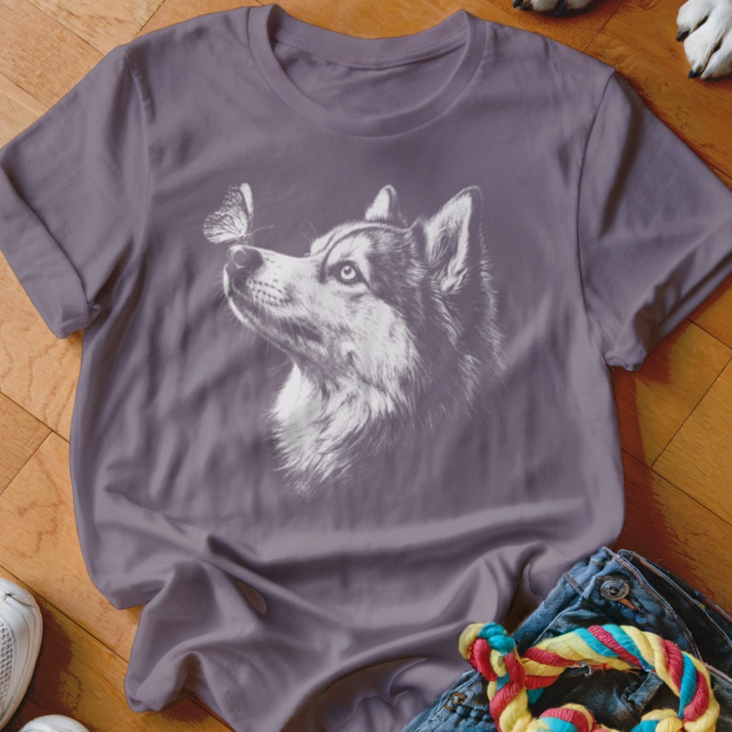A purple t-shirt featuring a white graphic of a husky looking at a butterfly on its nose.