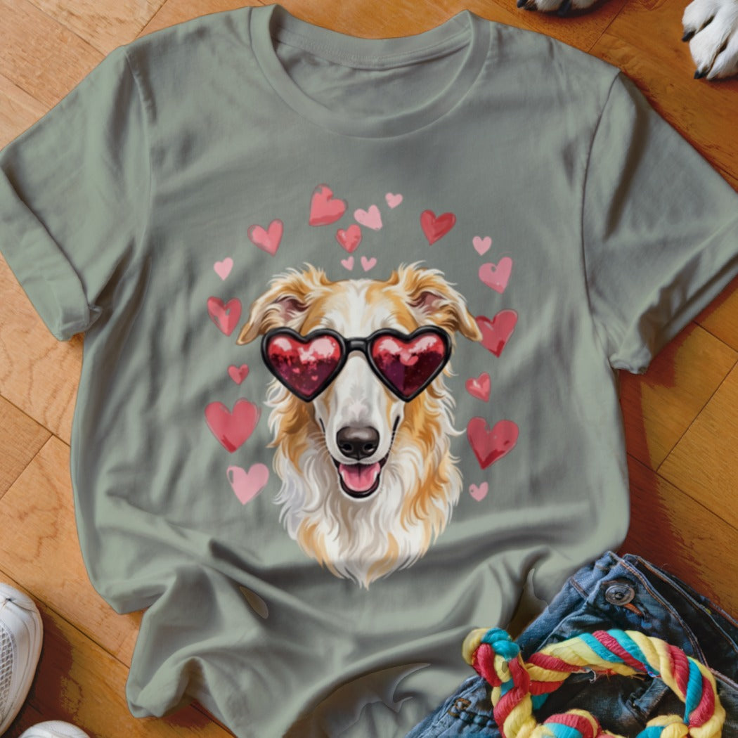 A sage green t-shirt featuring a graphic of a long-nosed dog wearing heart-shaped sunglasses surrounded by floating pink hearts.