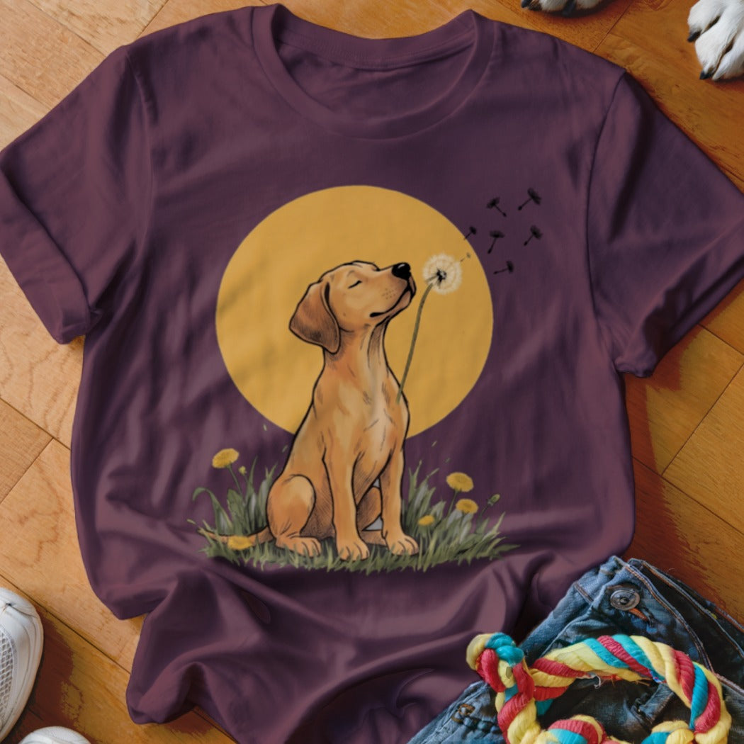 Dark maroon t-shirt featuring an illustrated yellow Labrador puppy blowing dandelion seeds against a golden moon.