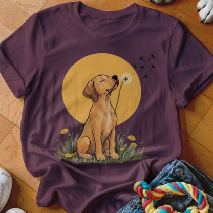 Dark maroon t-shirt featuring an illustrated yellow Labrador puppy blowing dandelion seeds against a golden moon.