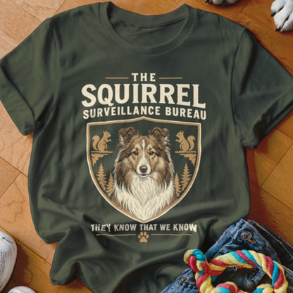 Dark green t-shirt with a graphic of a dog, squirrels, crest, and text reading The Squirrel Surveillance Bureau.