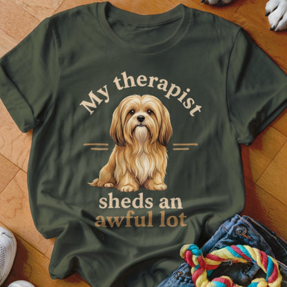 Olive green t-shirt with a fluffy dog illustration and text "My therapist sheds an awful lot".