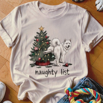 Light-colored t-shirt featuring a graphic of a white dog peeing on a Christmas tree, with the text naughty list.