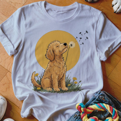 A white t-shirt featuring a graphic of a golden puppy blowing dandelion seeds against a yellow circle.