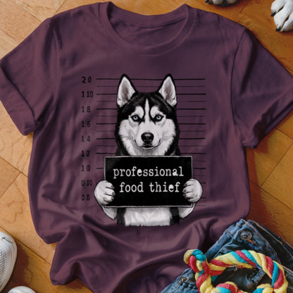 Husky holding a "professional food thief" sign in mugshot style on a dark red t-shirt.