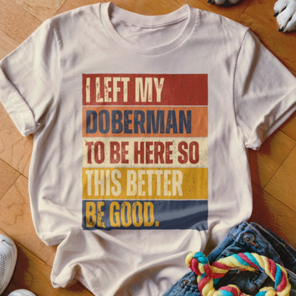 White t-shirt with retro text: "I LEFT MY DOBRMAN TO BE HERE SO THIS BETTER BE GOOD."