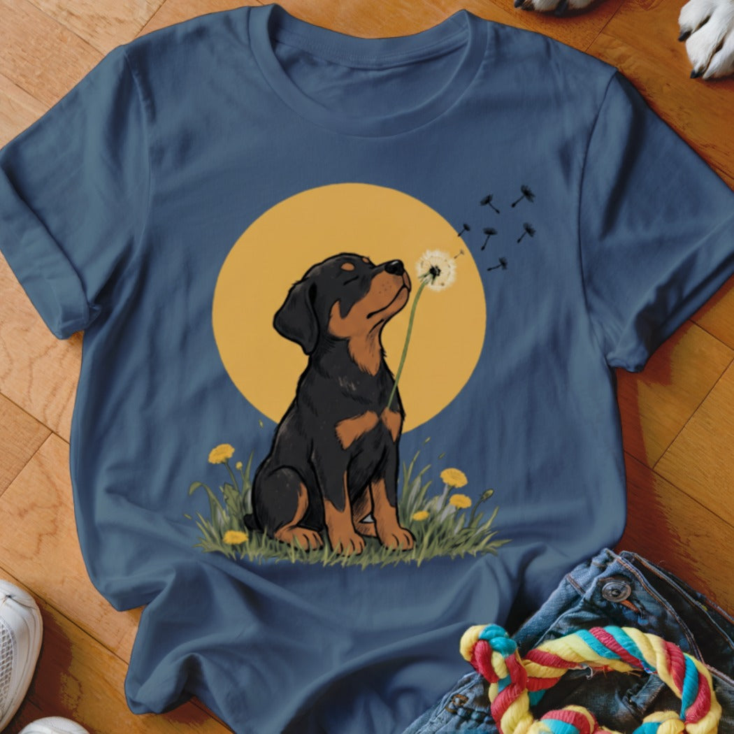 A blue crewneck t-shirt featuring a graphic of a Rottweiler puppy blowing dandelion seeds.