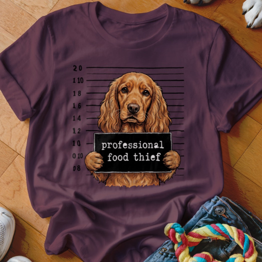 Cocker spaniel with a "professional food thief" sign against a mugshot background.