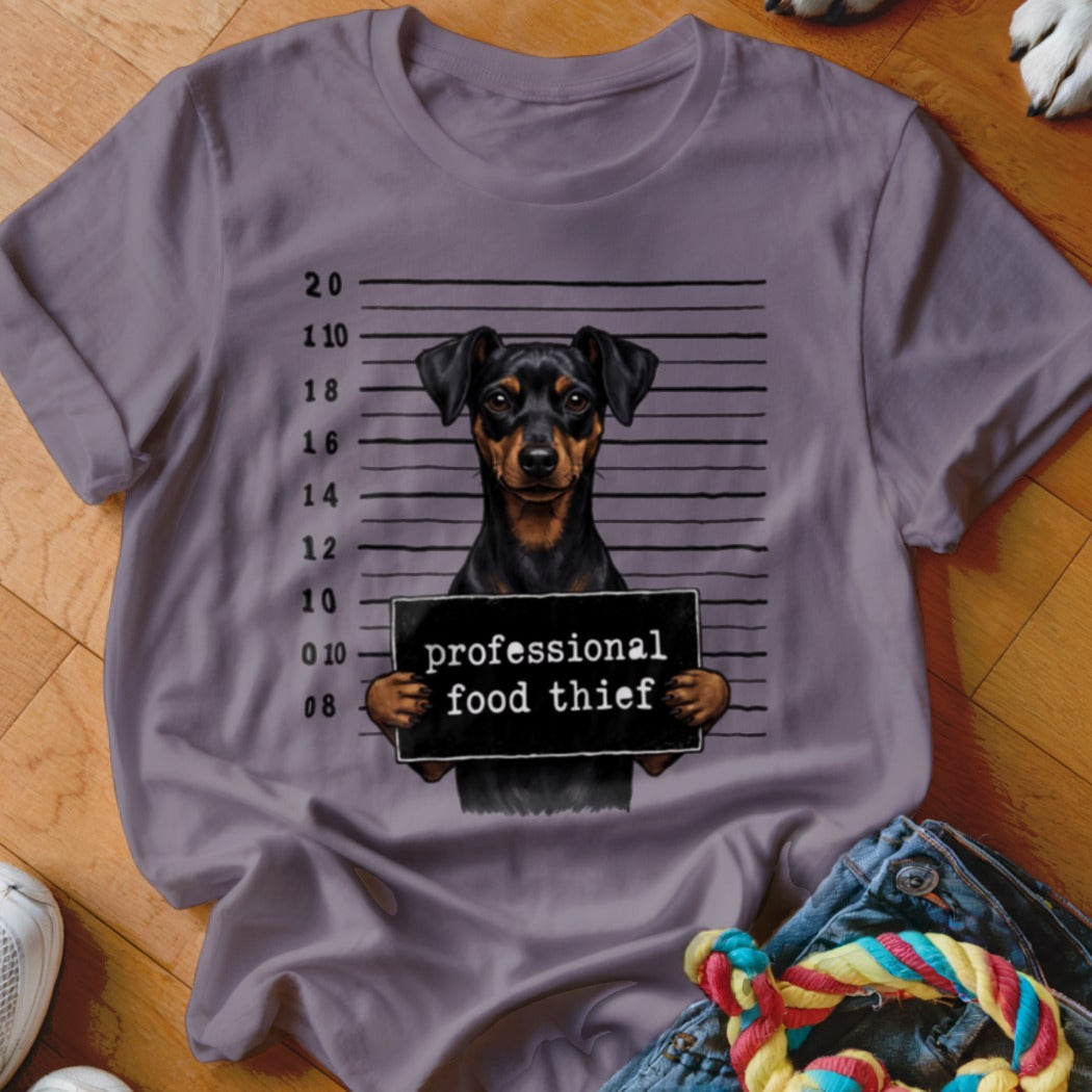 Dog mugshot with sign reading "professional food thief" on a purple t-shirt.