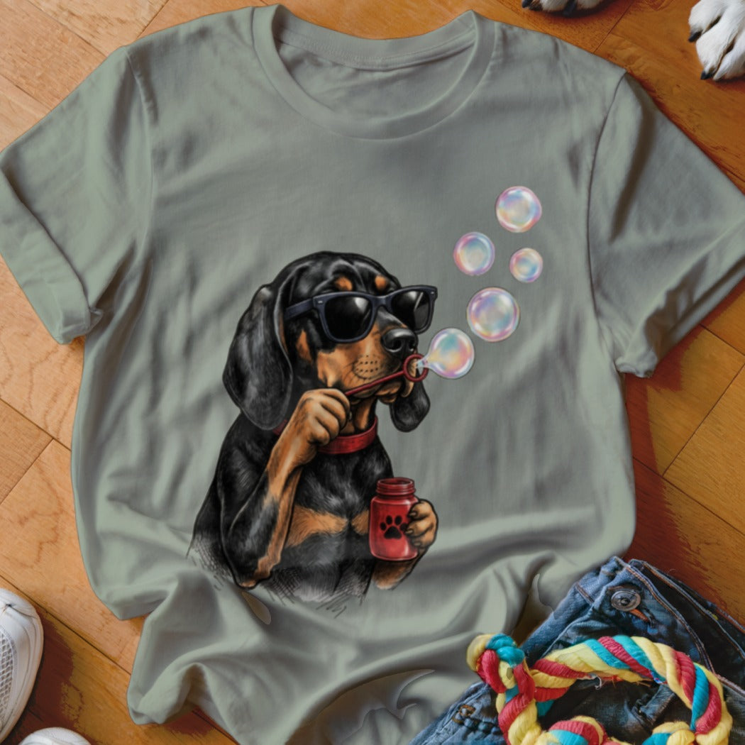 Sage green t-shirt featuring a graphic of a black and tan dog wearing sunglasses and blowing bubbles.