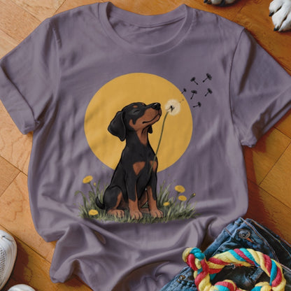 A purple short-sleeved t-shirt featuring an illustration of a black and tan puppy blowing dandelion seeds.