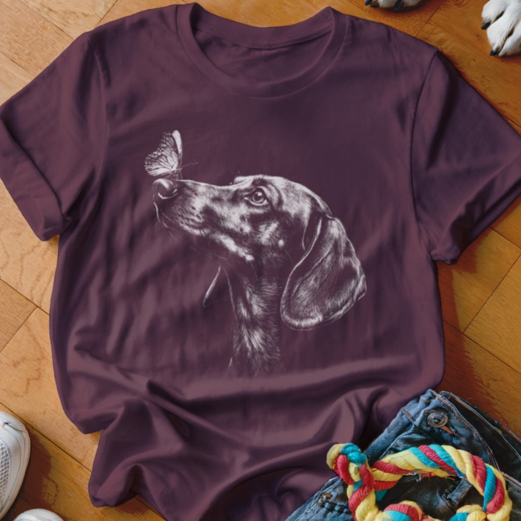 A dark purple t-shirt featuring a white sketch graphic of a dachshund looking at a butterfly.