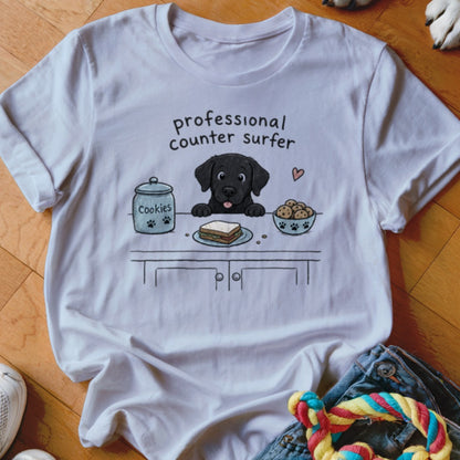 Black lab puppy on a counter with a cookie jar and sandwich, reading "professional counter surfer".