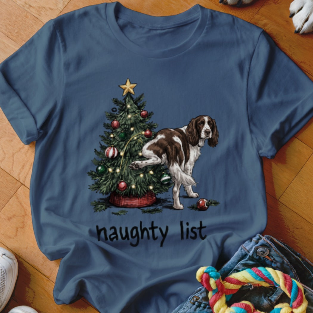 Brown and white dog lifting leg by decorated Christmas tree with "naughty list" text.