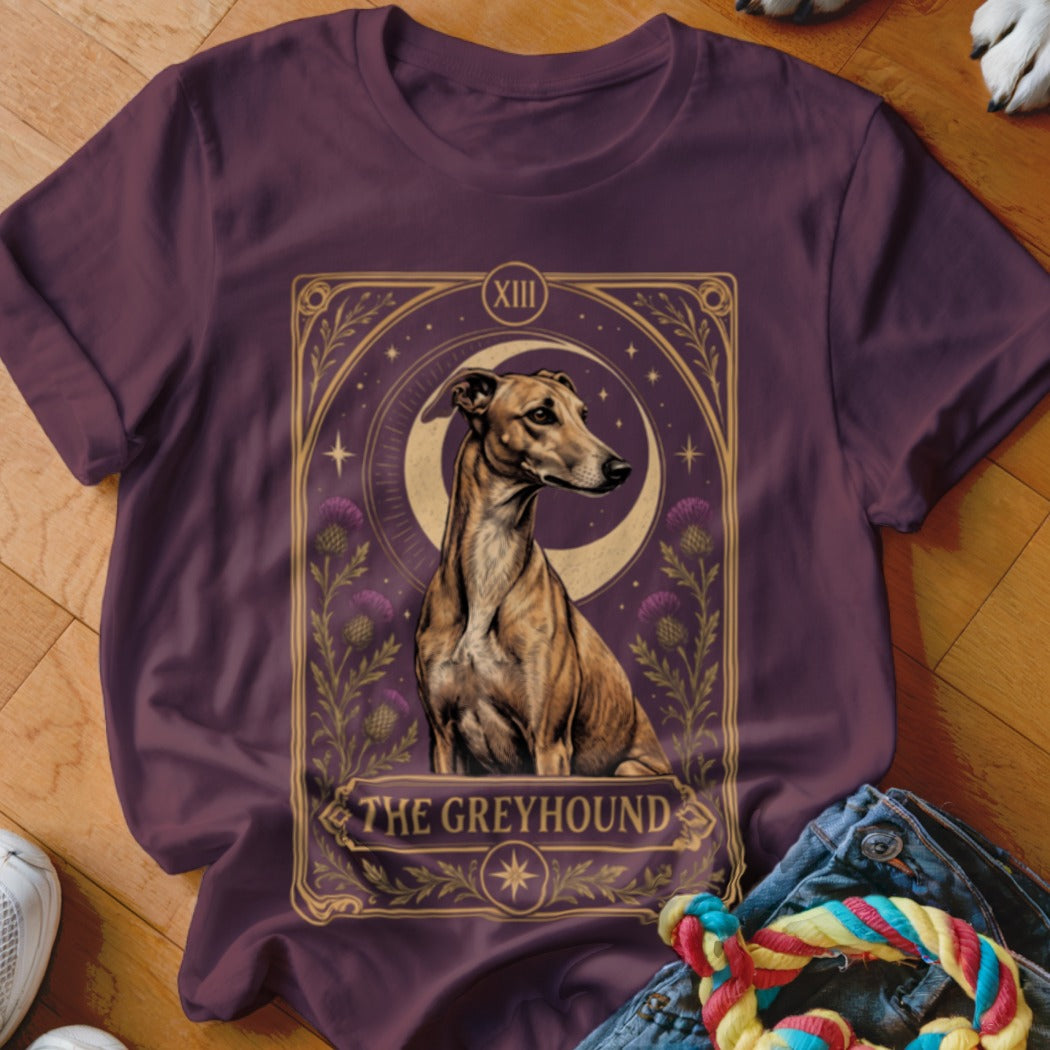 A plum-colored t-shirt features a tarot-style graphic of a brindle greyhound sitting before a crescent moon, framed by thistles and the text "THE GREYHOUND".
