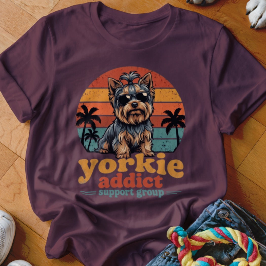 A dark purple t-shirt features a retro sunset graphic with a Yorkshire Terrier wearing sunglasses, palm trees, and text reading Yorkie addict support group.
