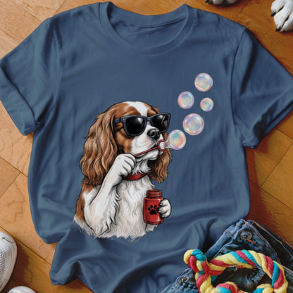 A dark blue t-shirt printed with a graphic of a Cavalier King Charles Spaniel wearing sunglasses and blowing soap bubbles.