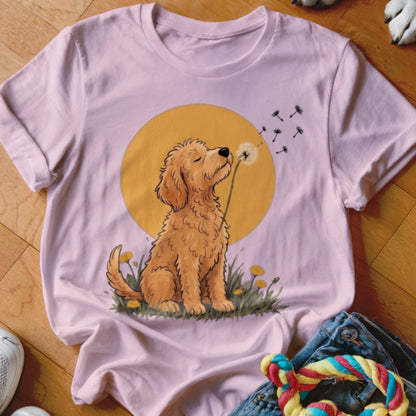 Pink t-shirt featuring an illustration of a golden doodle blowing dandelion seeds against a yellow circle background.