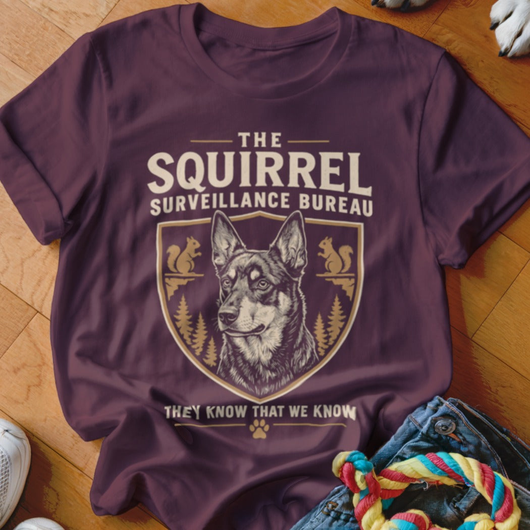Maroon t-shirt featuring a crest with a German Shepherd, squirrels, pine trees, and text reading The Squirrel Surveillance Bureau.