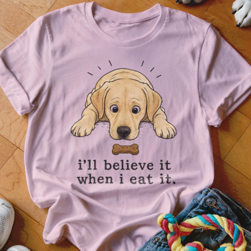 Pink t-shirt with a yellow lab puppy looking at a dog bone and text that reads "i'll believe it when i eat it."
