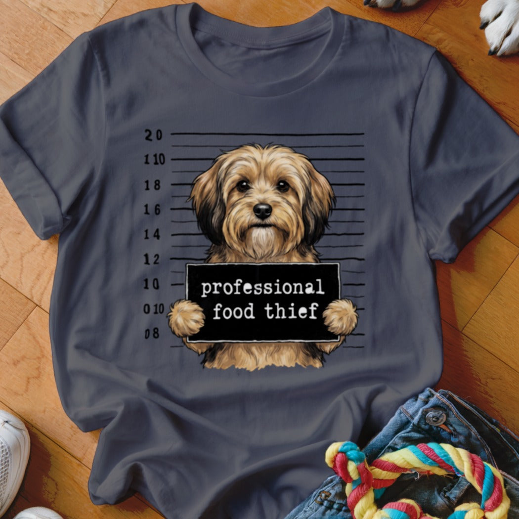 Fluffy dog mugshot with "professional food thief" sign on dark grey t-shirt.