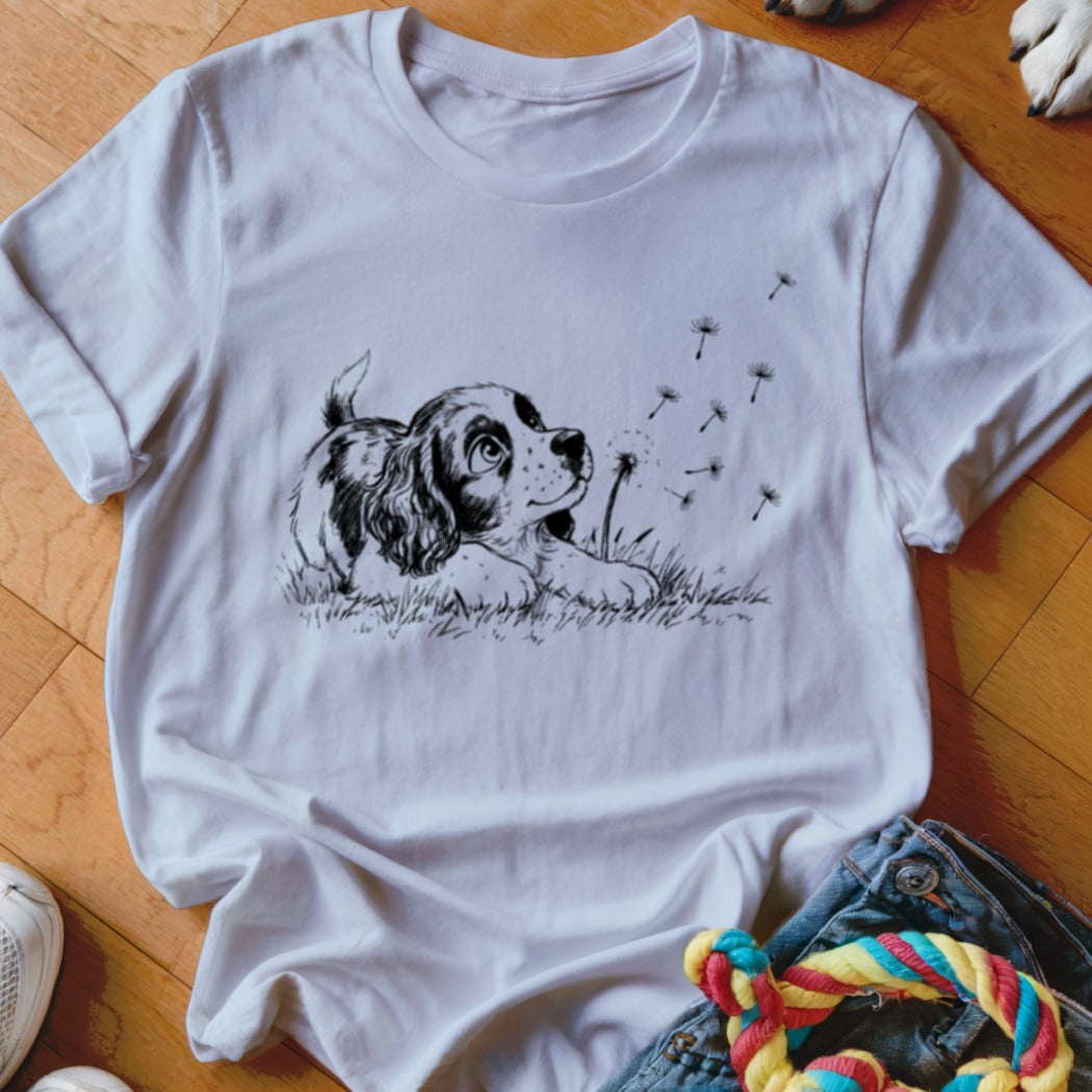 White t-shirt with a black line art graphic of a puppy watching dandelion seeds blow away.