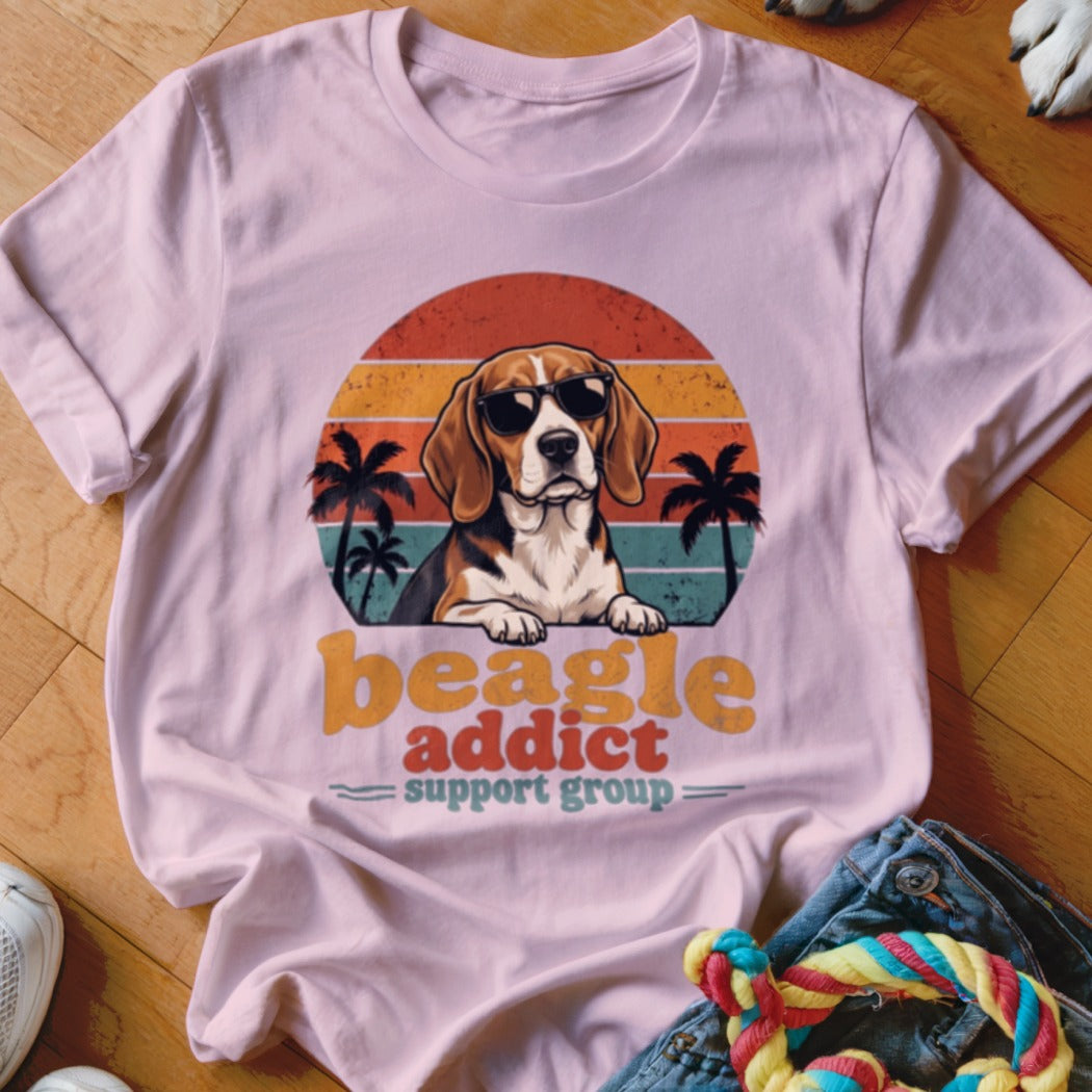 A pink t-shirt features a vintage graphic of a beagle wearing sunglasses in front of a sunset, palm trees, and the text "beagle addict support group."