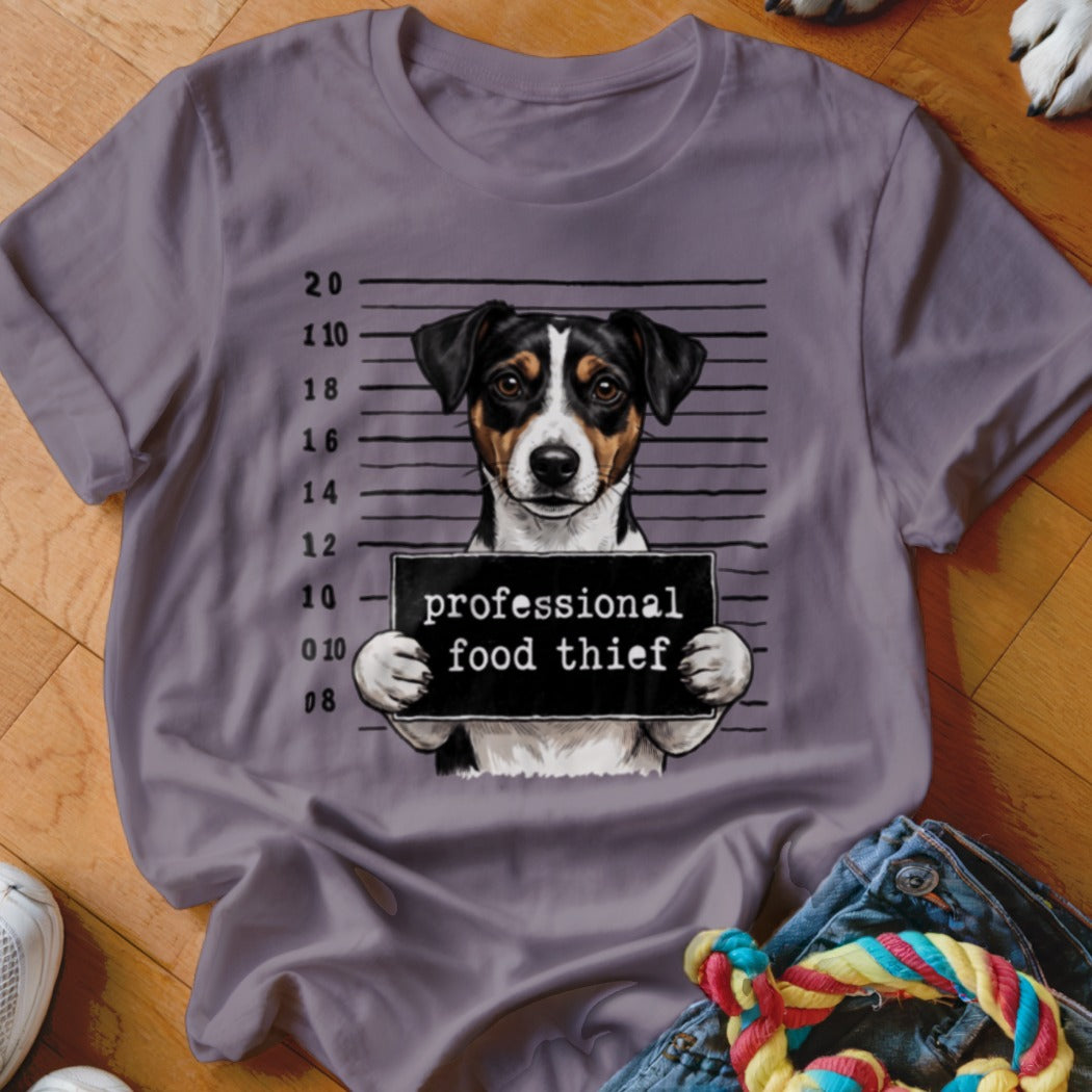 Dog mugshot with sign reading "professional food thief" on a purple t-shirt.