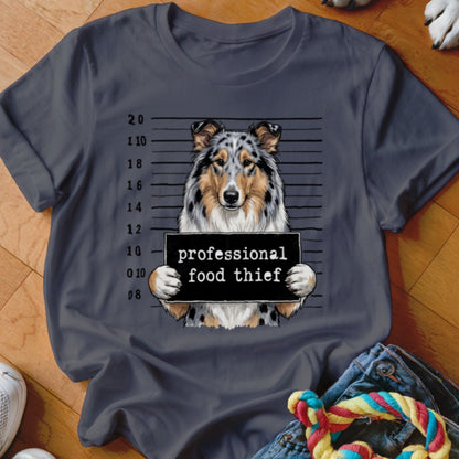 Collie dog mugshot with "professional food thief" sign on t-shirt.