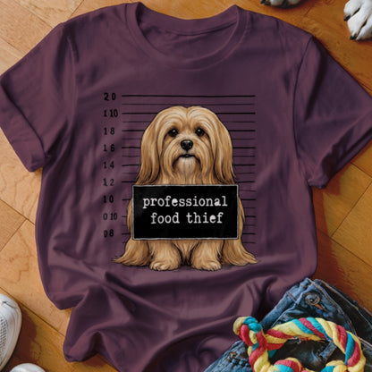 Fluffy dog in mugshot pose holding a "professional food thief" sign.