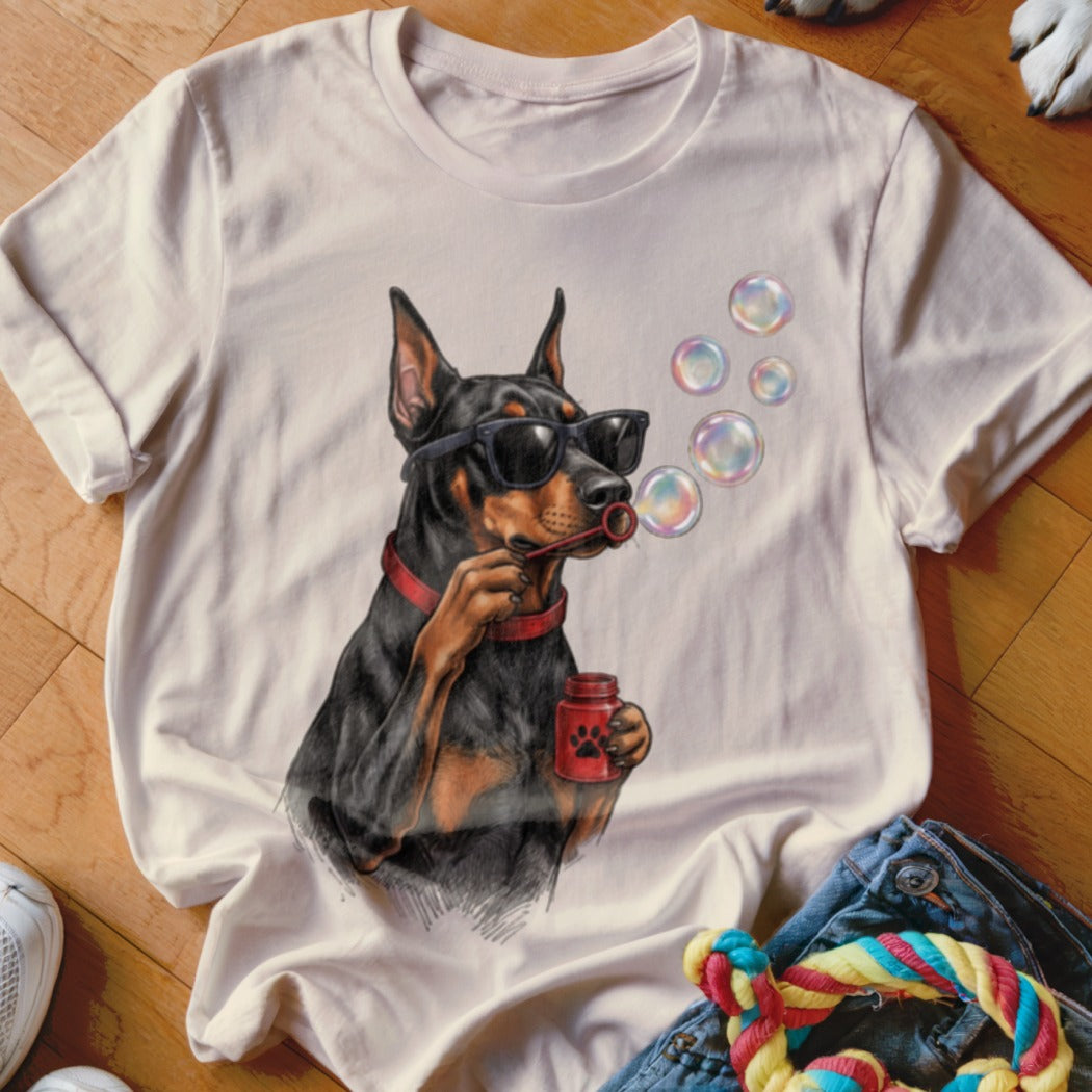 A light-colored t-shirt with a graphic of a Doberman wearing sunglasses and blowing bubbles.
