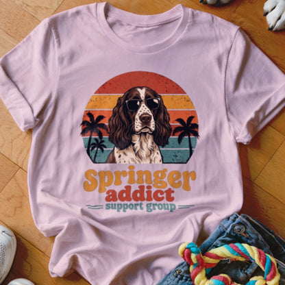 A light pink t-shirt with a graphic of a dog wearing sunglasses, palm trees, and text reading Springer addict support group.