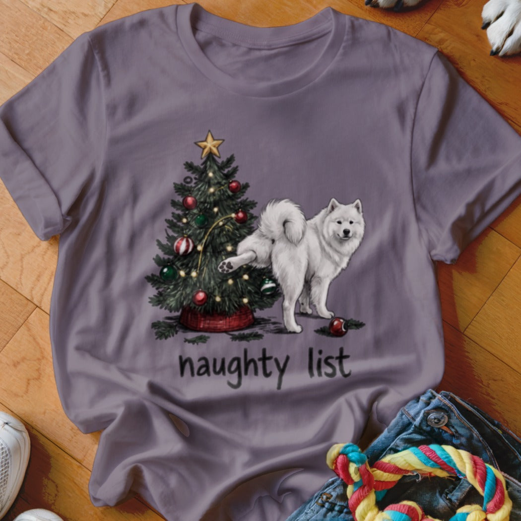 A grey t-shirt featuring an illustration of a white Samoyed lifting its leg on a decorated Christmas tree above the text naughty list.