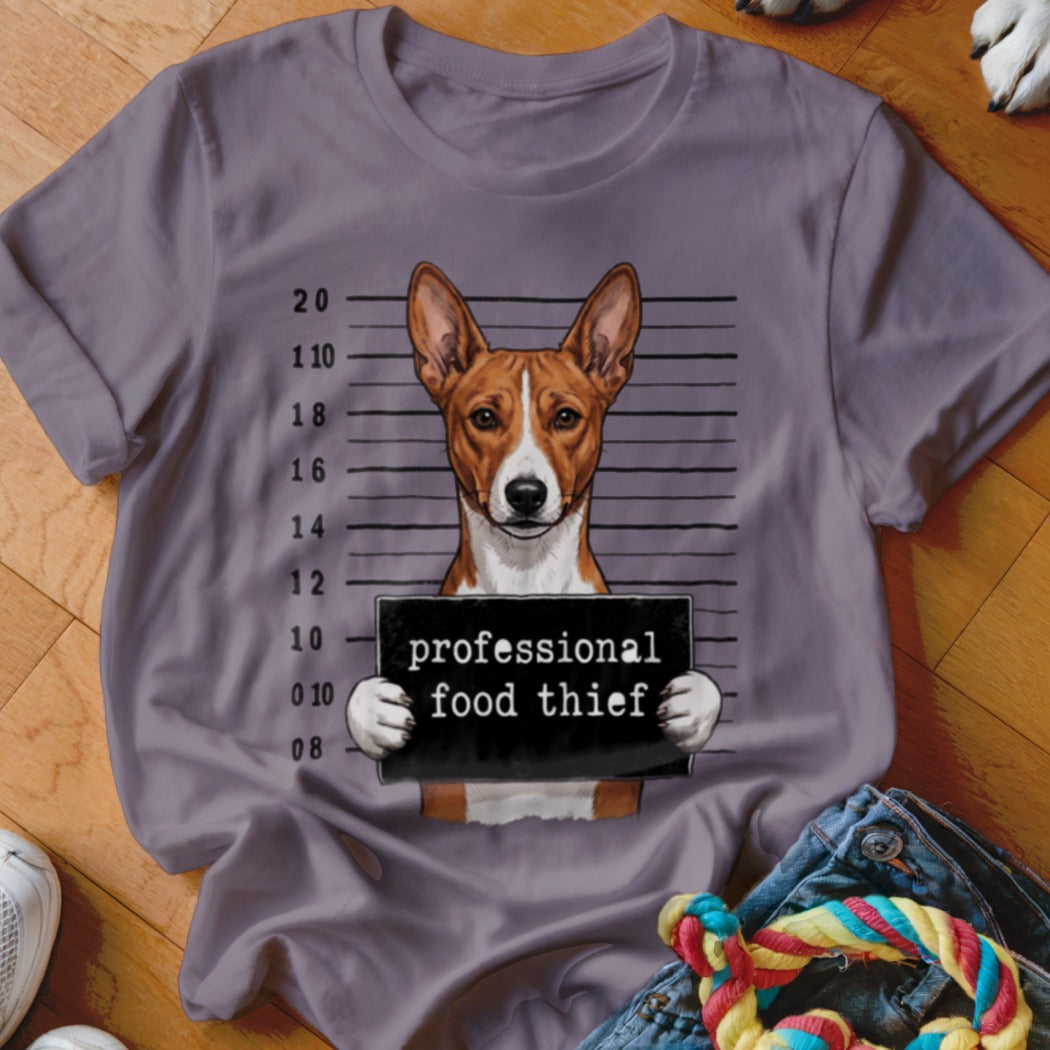 Basenji dog mugshot with "professional food thief" sign on purple t-shirt.