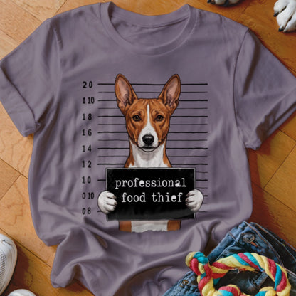Basenji dog mugshot with "professional food thief" sign on purple t-shirt.