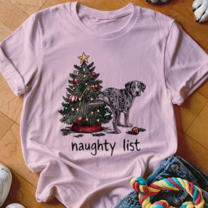 A light pink t-shirt displays an illustration of a spotted dog lifting its leg against a decorated Christmas tree, with the text "naughty list" below.