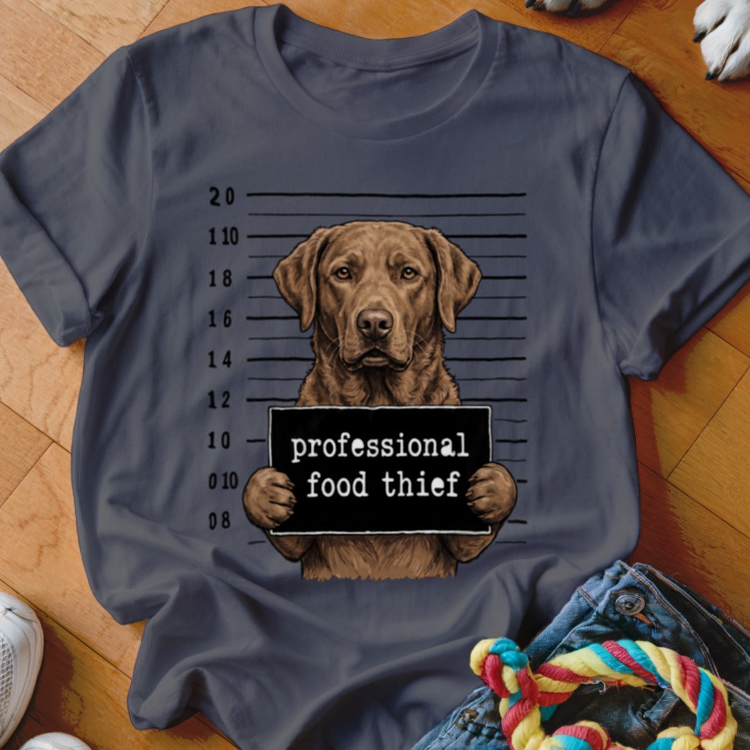 Labrador Retriever mugshot with "professional food thief" sign on t-shirt.