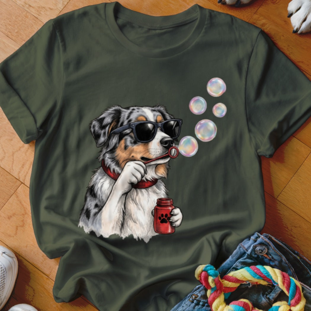 An olive green t-shirt featuring a graphic of an Australian Shepherd wearing sunglasses and blowing bubbles.