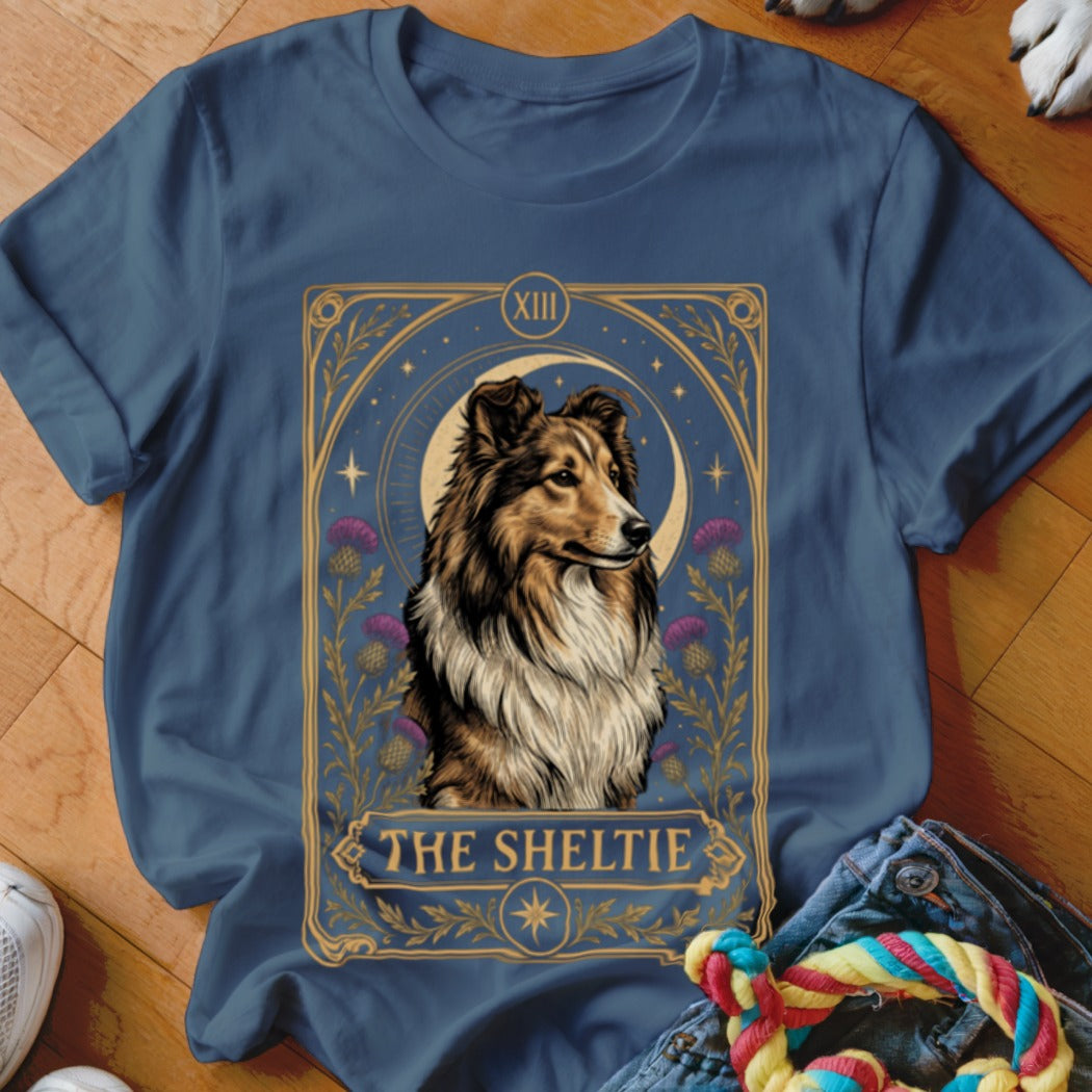A dark blue t-shirt featuring a tarot card graphic of a Sheltie dog and purple flowers.
