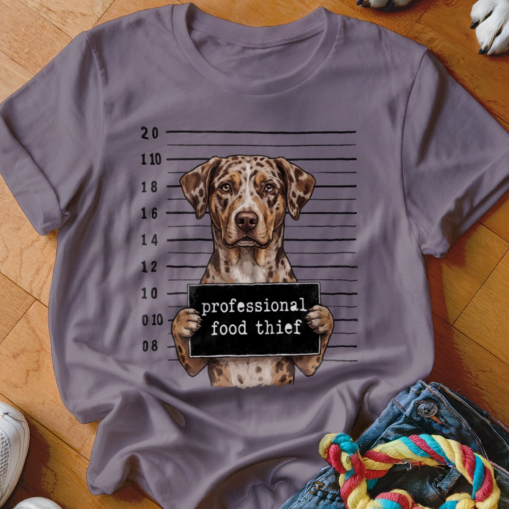 Dog mugshot with "professional food thief" sign on a grey t-shirt.