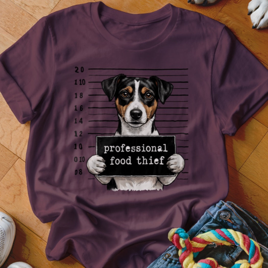 Jack Russell Terrier mugshot with "professional food thief" sign on t-shirt.