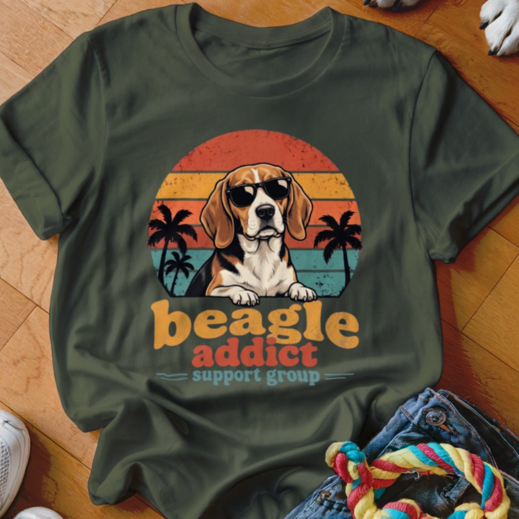 An olive green t-shirt with a graphic of a beagle wearing sunglasses in front of a sunset, with text reading "beagle addict support group."