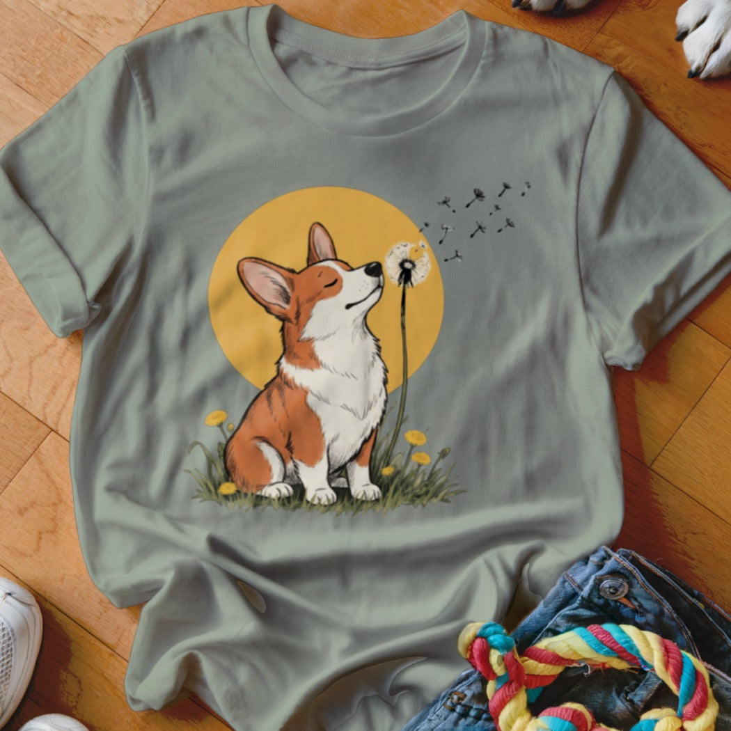 A sage green crewneck t-shirt featuring a graphic of a corgi blowing a dandelion against a yellow circle.