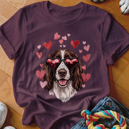 A dark plum t-shirt featuring a graphic of a brown and white dog wearing heart-shaped sunglasses, surrounded by floating hearts.