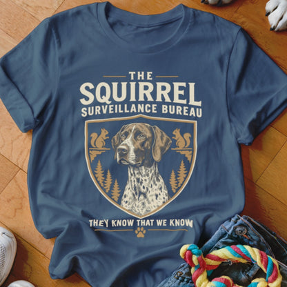 Blue t-shirt featuring a crest with a pointer dog, pine trees, squirrels, and text reading The Squirrel Surveillance Bureau.