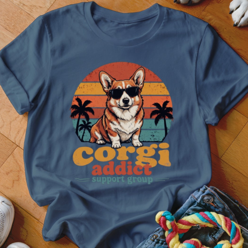 Blue t-shirt featuring a retro graphic of a corgi in sunglasses with palm trees and sunset.