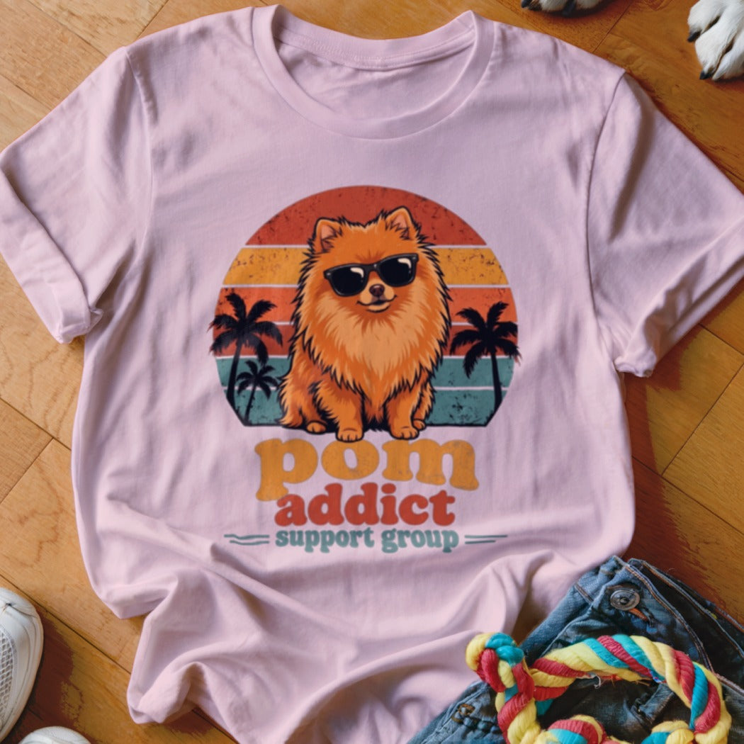 Light pink t-shirt featuring a retro sunset graphic, a Pomeranian wearing sunglasses, and the text pom addict support group.