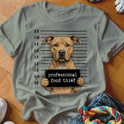 Tan pit bull mugshot with "professional food thief" sign on gray t-shirt.