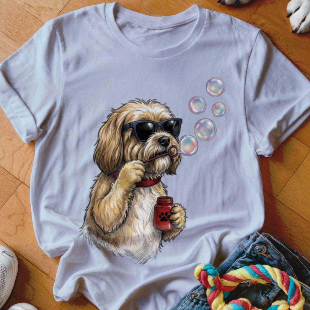 A white t-shirt featuring an illustration of a fluffy golden dog wearing sunglasses and blowing soap bubbles.
